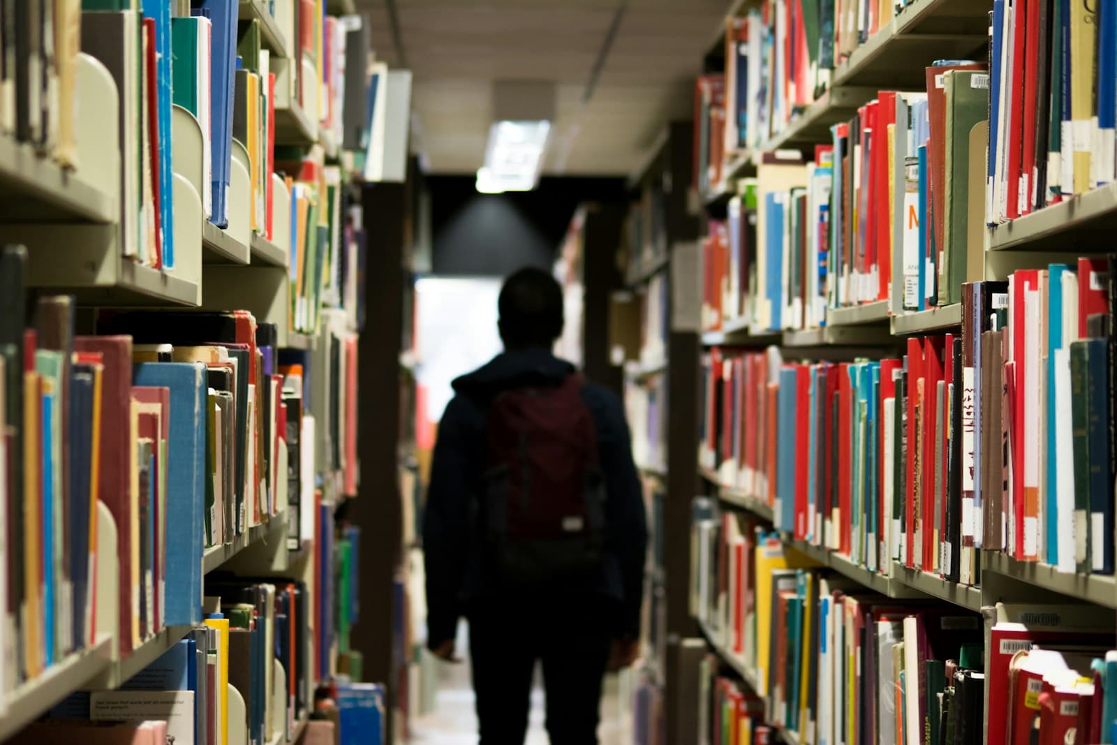 A person with a backpack walking between library shelves
