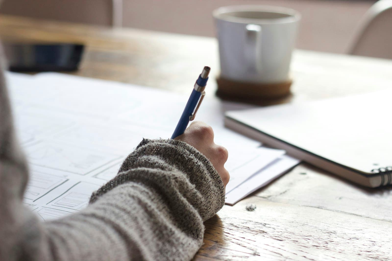 A hand sketching screen layouts on paper at a wooden table