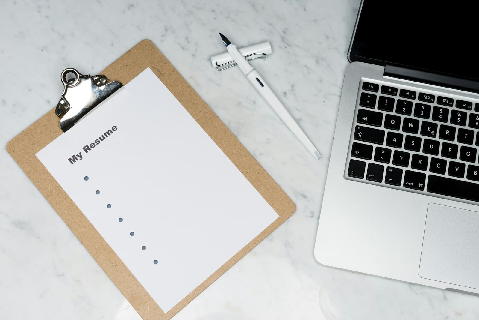 A clipboard labeled resume next to a laptop and a pen